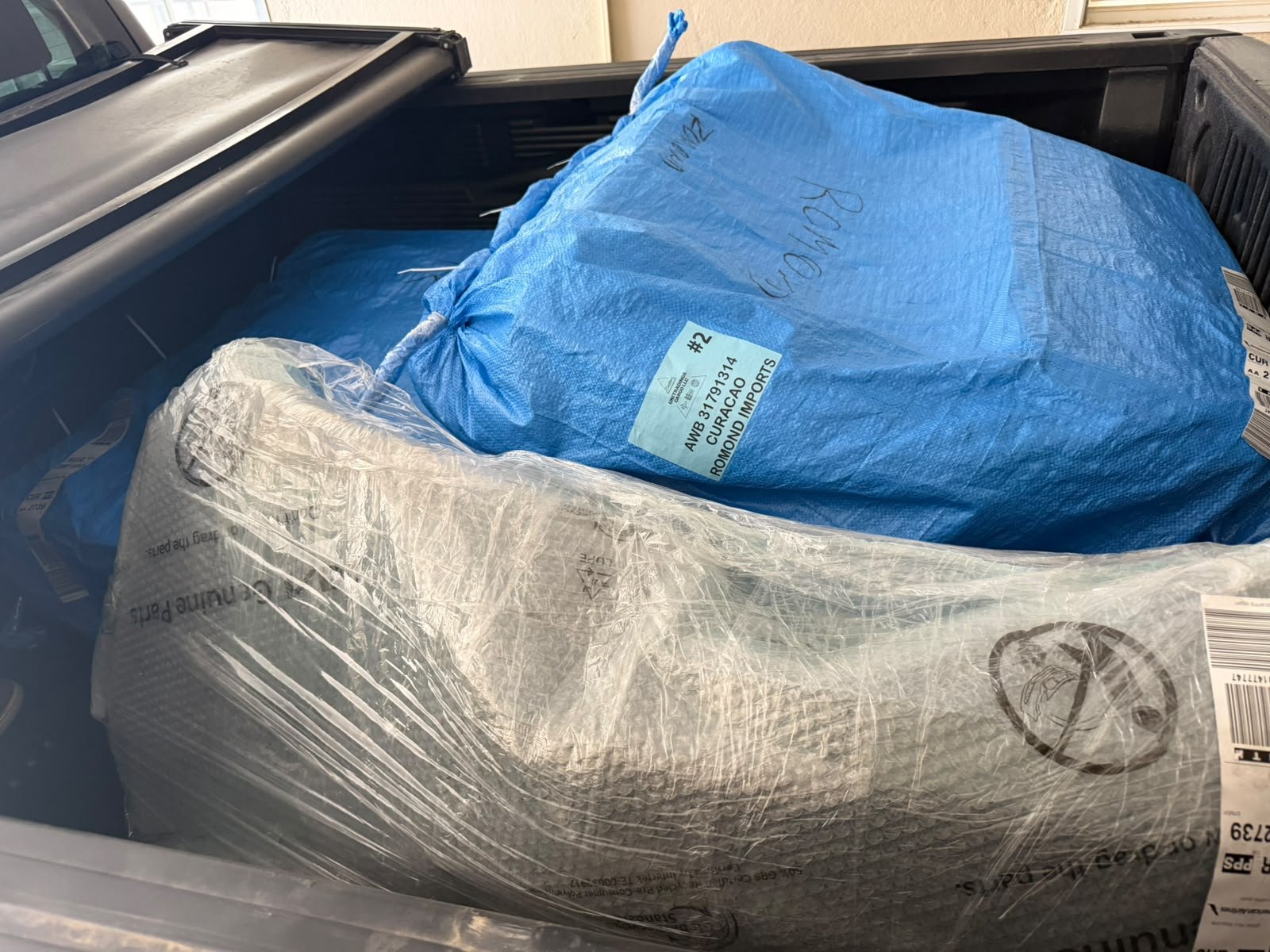 Romond Imports air freight packages and a bubble-wrapped car part in a pickup truck bed